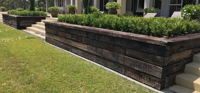 lawn with raised retaining wall with sleepers and shubery behind