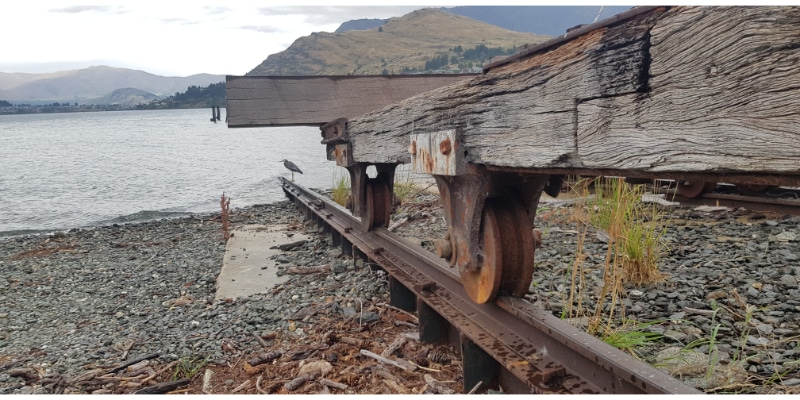 rail track with hardwood beam on steel wheel with lake and mountians in background.