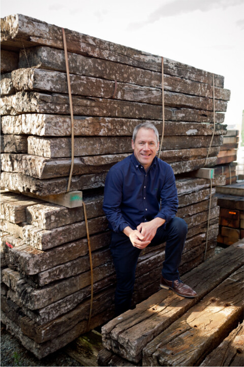 A man leaning against a stack of wooden planks.